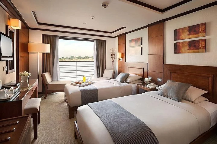A twin-bed cruise cabin with a seating area and a view of the Nile