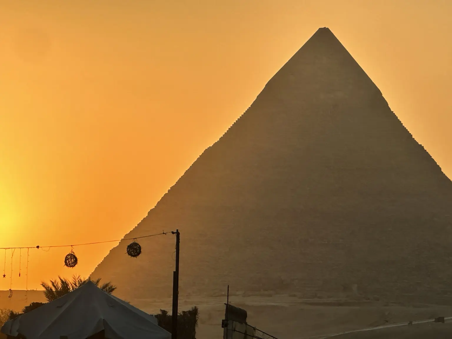 A pyramid silhouetted against a deep golden Egyptian sunset